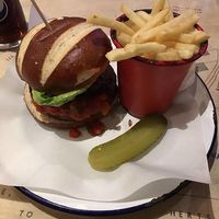 A delicious bean burger (marked VG on the menu) with fries. The burger is topped with salsa, a flat mushroom, a tomato and lettuce, served in a pretzel bun. The fries are amazing.  at The Woolpack in Hertford