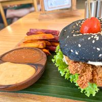 Fried Chickenless Burger – crispy battered oyster mushrooms on a charcoal bun with slaw and vegan mayo, served with baked sweet potato fries tomato sauce, and sambal mayo at Dharma Coffee & Juice in Ubud
