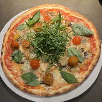 Pizza Sebastian with tomato sauce, vegan cheese, mushrooms, potatoes, basil, salad rocket, and chili oil.  at Café Piccolina in Aarhus
