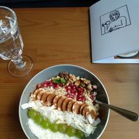 Coconut yoghurt breakfast bowl with banana, coconut, oats, grapes, pomegranate seeds, nuts and maple syrup. at Panenská Kaviareň in Bratislava