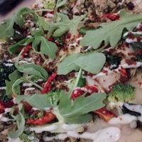 close up of the pesto chicken CBR pizza with aragula, garlic ranch dressing, broccoli at Virtuous Pie in Toronto