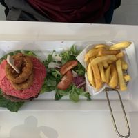 Cheese burger with bacon served on a beetroot bun and a side of chips, salad and onion rings  at Naked Bakery in Edinburgh