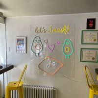 Light up sign depicting two anthropomorphized avocados and bread reading “let’s smash!” at Root in Newport