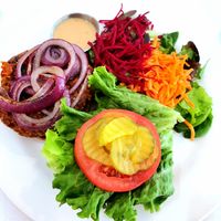 Burger with fresh veggies, grains, and grilled onions on a sprouted bun at Ananda Fuara in San Francisco
