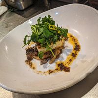 Griddled turnip rice cake over miso clamshell & oyster mushrooms, drizzled w/ fermented black bean chile orange oil, topped w/ pea shoot-pickled ginger-shredded snap pea salad. at Millennium in Oakland