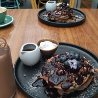Blueberry buckwheat pancakes with whipped coconut cream and maple syrup, peanut butter cacao smoothie on the left  at Boneless Vegetarian Cafe in Bermagui