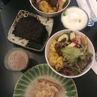 Two small bowls, matcha latte (top right), chai latte (bottom left), black sesame cake, and passion fruit and almond cake  at Tushita in Munich