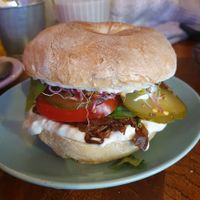 Marinated oyster mushroom (wheat bagel) with soy mayo, pickled cucumber, tomatoes, sprouts, and fresh spinach at Avocado Spot in Gdansk