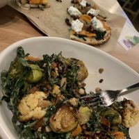 seasonal ingredient salad (vegan) in foreground, with butternut squash pizza with almond ricotta (vegan) in background at True Food Kitchen in Oakbrook