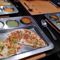 Mixed vegetable uthappam in foreground surrounded by two dosa and one invisible thali at Krishna Vilas in Eindhoven