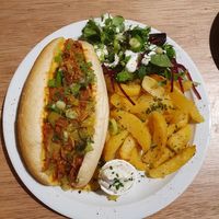 Hotdog bun filled with minced meat in dill sauce, melted cheddar, pickles, caramelized onions and side of roasted
potatoes and salad with ranch sauce at Lucifer Lives in Brussels