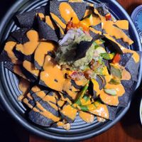 Nachos - Looks good. Tastes terrible. The "cheese sauce" is like orange oil. They have no beans except edamame which I ordered separately. It's mainly chips and oily orange sauce. at The Honu in Dunedin