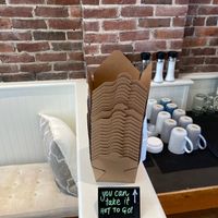 Pile of takeout containers with a sign reading YOU CAN TAKE IT HOT TO GO 🔥 at Mixed Greens in Camden