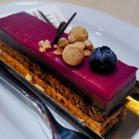 This vegan cake has four layers. At the bottom a crunchy nougat, then cake, then chocolate mouse, and finally a layer of gelled berries. It is topped with some nuts, a black berry  at Zenhäusern in Sierre
