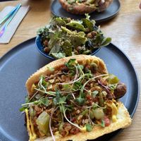 Brunch dog with mung bean scrambled “eggs”, salsa verde with avocado, tofu bacon, potato crisps, cucumber pickles, greens, tofu hollandaise with a side “no parm no foul” sa at Good Dogs Plant Foods in Vancouver