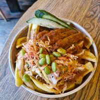 vegan chicken katsu loaded fries: crispy vegan chicken tenders, cucumber, ginger & sesame shredded cabbage, edamame & katsu sauce on canoe cut fries at Wolf at the Door in Manchester