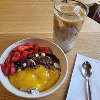 Overnight oats with coconut milk, mango puree, granola and berries. And vegan iced latte. at Freddy's Cafe in Kolding