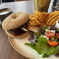 Falafel in a sesame bagel with hummus and vegan tatziki. Oat milk flat white in the back  at WASBAR in Bruges