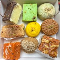 Box of Indian sweets. First row from the top from the left: chocolate barfi, pista (chio) barfi, Ghari. Second row from the top from the left: Mawa Milk Cake, Kesar Penda, Mawa Penda. Third row from the top: carrot barfi, Churma Ladoo, Habshi Halwa. at RK Dining in Preston