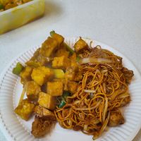 Tofu satay and "chicken" chow mein on a paper plate for eating in at Wawin Vegan Chinese in Sheffield