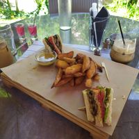 Half-eaten vegan club Sandwich with roasted veggies and vegan sauce. Crispy country potatoes and coffee wth almond milk. at Enasma Cafe in Crete