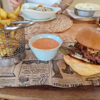 Hamburguesa vegana de beyond burguer. Es de pequeño tamaño pero está muy buena. Lleva lechuga, tomate, cebolla crujiente y una salsa. Las patatas llevan una salsa picante. Segú at Cala Petita in Mallorca