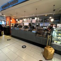 Exterior and has communal seating plus small tables and chairs  at LCY - Caffe Nero in East London