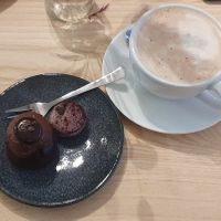 A chocolate brownie with chocolate mousse with chocolate on top, a blueberry macaron and a hot chocolate. at ima vegan  in Hamburg