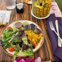 A variety of the buffet food that is vegan including vegetables, rice, fruit and salad. Plus a mango vegan drink in a pineapple.   at Polynesian Cultural Center in Laiea