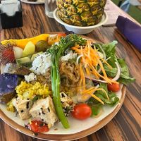 A variety of the buffet food that is vegan including vegetables, rice, fruit and salad. Plus a mango vegan drink in a pineapple.   at Polynesian Cultural Center in Laiea