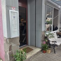 Eingangsbereich mit Pflanzen. Auf dem Bürger*innensteig vor dem Laden stehen Tische und Stühle und eine bequeme Bank. at Nunu Mannheim in Mannheim