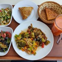 Two salads on the left, one pumpkin somsa and some flatbread on top, two veggie mains on the large plate, and fresh carrot juice. at Do'stlar in Tashkent