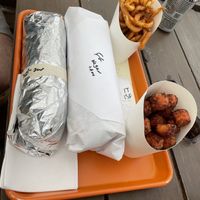 Huge falafel sandwich (white paper) with side of curly fries and sweet potato tots  at Eastcut Sandwich Bar in Durham