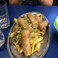 Salchichas al vino. 100% recomendable. Un plato con salchichas sazonadas con especias y vino adobadas con guisantes y cebolla sobre una capa de patatas fritas.   at B13 Bar in Madrid