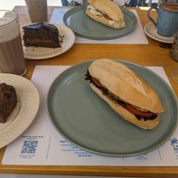 Fatia de bolo de banana com gotas de chocolate, pão de melado, sanduíche de tempe, macchiato de doce de leite, vitamina protéica, sanduíche de tofu minas e capuccino at Casa Madal in Sao Paulo