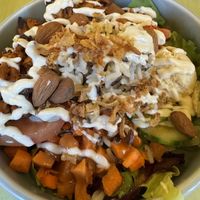 Eine bunte Bowl mit Salatbasis, Reismix, Gurkenscheiben, Tomaten, gewürfelter Karotte und einer cremigen Hummus-Nocke; obendrauf geröstete Mandeln und Röstzwiebeln.  at Katzentempel - Freiburg in Freiburg