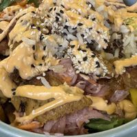 Herzhaft belegte Bowl mit Blattsalat, Reis, eingelegtem rosa Gemüse, knusprig angebratenen pflanzlichen Streifen und einem Sesam-Mix; darüber eine würzig-orange Sauce.  at Katzentempel - Freiburg in Freiburg