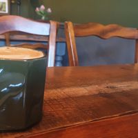 A green mug with a foamy flat white, on a wooden table at The Kitchen Treasury in Kirkcaldy