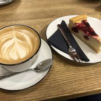 Cappucino (Hafermilch) mit Himbeer-Creme Kuchen/ cappucino (oat milk) with raspberry-cream cake  at Mayersche   in Cologne