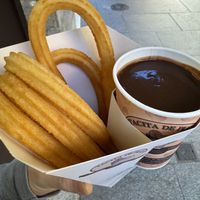 A to-go container holding churros and a cup of chocolatee  at Tacita De Plata in Madrid