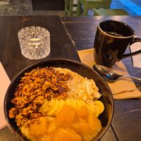 Porrige with mango compott, coconut, granola and banana. Served with hot foamed  oat milk. at Grain Café in Stockholm