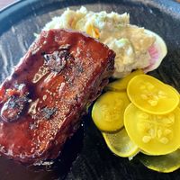 Whiskey and cola rib plate with Mimi’s potato salad, squash, and Vidalia, pickles and radish. The sauce is a house made whiskey and cola black pepper barbecue sauce.  at Marian Cocktails and Kitchen in Raleigh