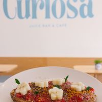 100% Vegan: Creamy almond butter, fresh raspberry and chia compote, sprinkled with bee pollen and cinnamon, topped with banana slices, on toasted sourdough bread. at Curiosa | Cafe & Juice Bar in Mexico City