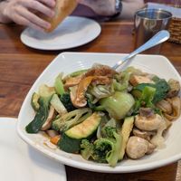 Vegetable chow fun dish, with a tofu banh mi being munched on in the background. at Blossom Vegan Restaurant in Pleasanton