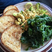 Breakfast scramble served w/ garlic-steamed greens & brown rice toast, seasoned tofu, green peppers, onions, mushrooms, broccoli, & carrots. Vegan cheese blended into seasoned tofu, scrambled w/green peppers onions, & mushrooms topped w/tomatoes. at The Wayward Cafe in Seattle