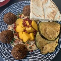 Mango and falafel plate with eggplant, hummus, pita, and pomegranate seeds  at Mango Vegan Street Food - Bracka in Warsaw