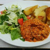 Vegan tofu bolognese sauce with potato wedges and salad garnish at Torschenke in Zons