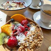 In alto porridge con latte vegetale, granola, banana e burro di frutta secca. In basso yogurt di soia naturale con granola, frutta fresca di stagione, semi e frutta secca.  at Paper Plane in Nice