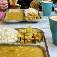 Two metal trays with dahl, rice and vegetables. Juice in two cups  at Thenga Cafe in London
