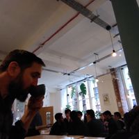 A bearded man sips in front of big windows. at Idle Hands in Manchester